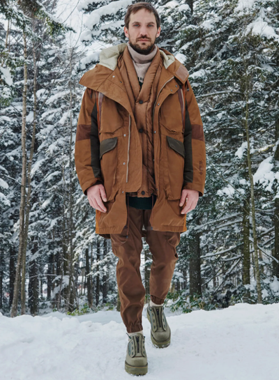 A man wearing a layered brown White Mountaineering outfit with two brown jackets and matching brown pants