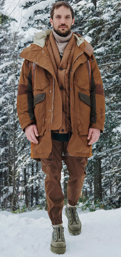 A man wearing a layered brown White Mountaineering outfit with two brown jackets and matching brown pants