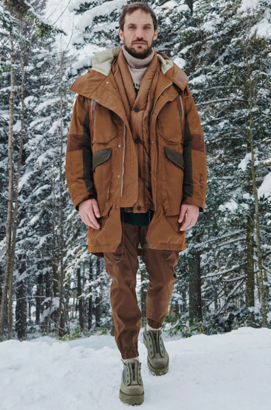 A man wearing a layered brown White Mountaineering outfit with two brown jackets and matching brown pants