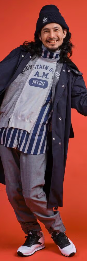 A man wearing a Mountain Research outfit featuring a double zip hoodie, navy blue overcoat and grey pants