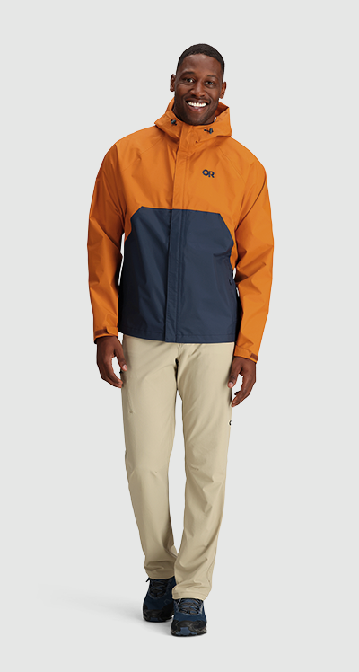 A man wearing an orange and navy blue Outdoor Research Jacket and beige pants