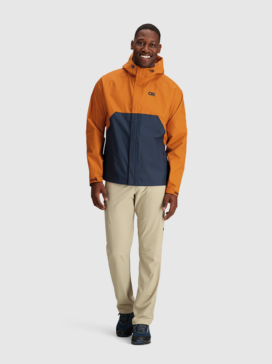 A man wearing an orange and navy blue Outdoor Research Jacket and beige pants
