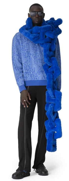 A man wearing a Piéces Uniqes outfit feauring an oversize blue pillow-like scarf and navy blue pants