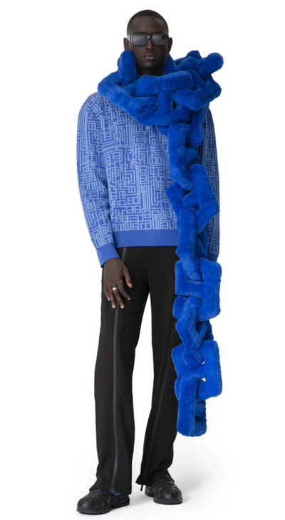 A man wearing a Piéces Uniqes outfit feauring an oversize blue pillow-like scarf and navy blue pants