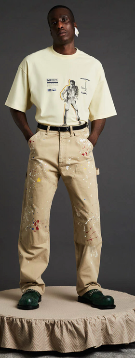 A man wearing a Martine Rose beige graphic t-shirt with brown pants