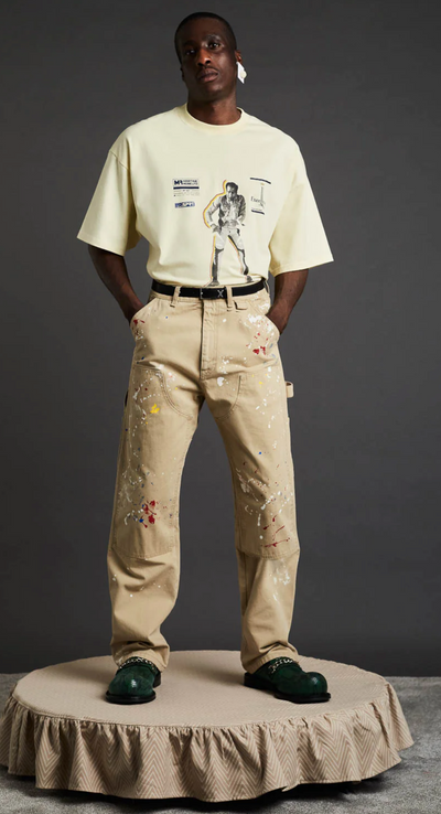 A man wearing a Martine Rose beige graphic t-shirt with brown pants