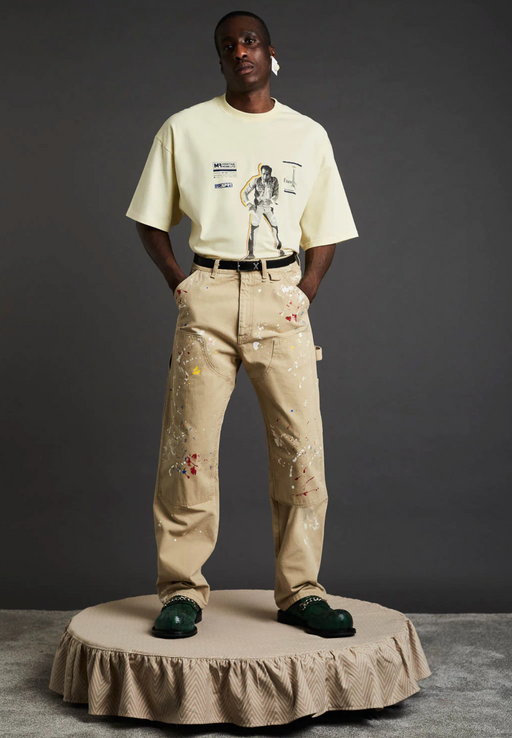 A man wearing a Martine Rose beige graphic t-shirt with brown pants