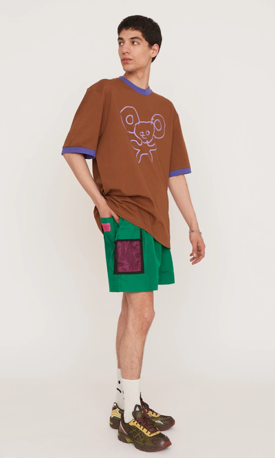 A man wearing a Lazy Oaf brown shirt and green shorts