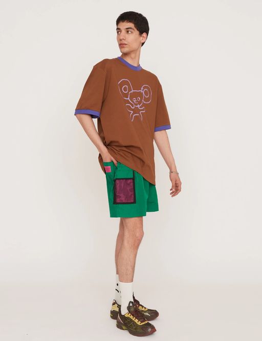 A man wearing a Lazy Oaf brown shirt and green shorts