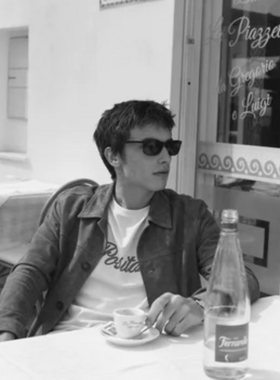 A man wearing a Harmony Paris t-shirt, jacket and sunglasses while having a cappucino