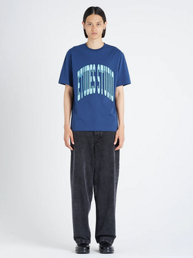 A woman wearing an Etudes Studio Logo shirt in blue and baggy pants