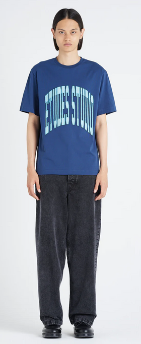 A woman wearing an Etudes Studio Logo shirt in blue and baggy pants