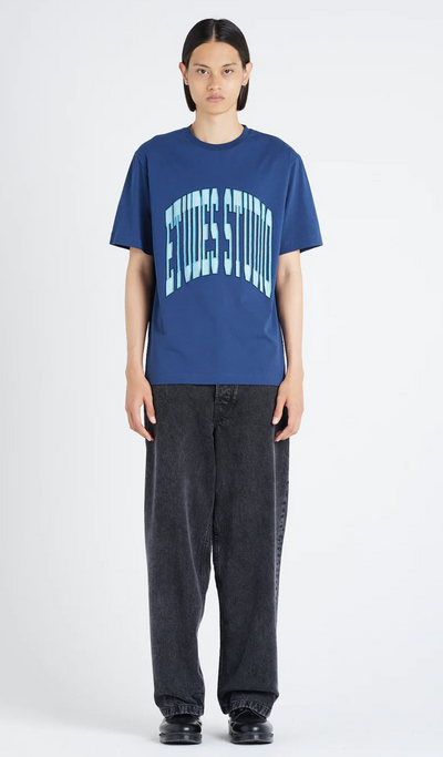 A woman wearing an Etudes Studio Logo shirt in blue and baggy pants
