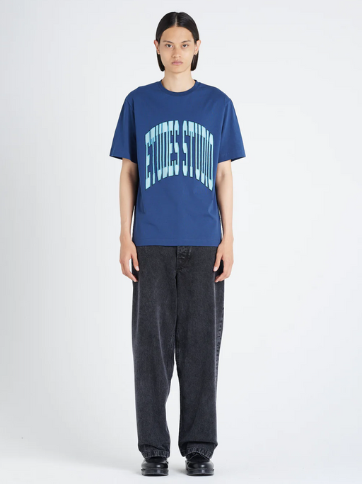 A woman wearing an Etudes Studio Logo shirt in blue and baggy pants
