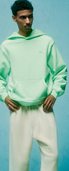 A man wearing a light green Madhappy hoodie and white sweatpants