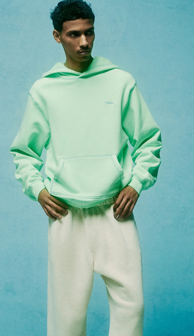 A man wearing a light green Madhappy hoodie and white sweatpants