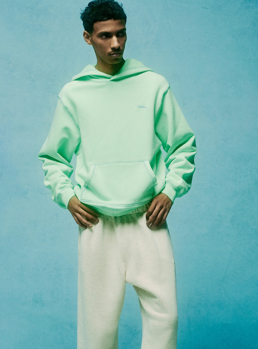 A man wearing a light green Madhappy hoodie and white sweatpants