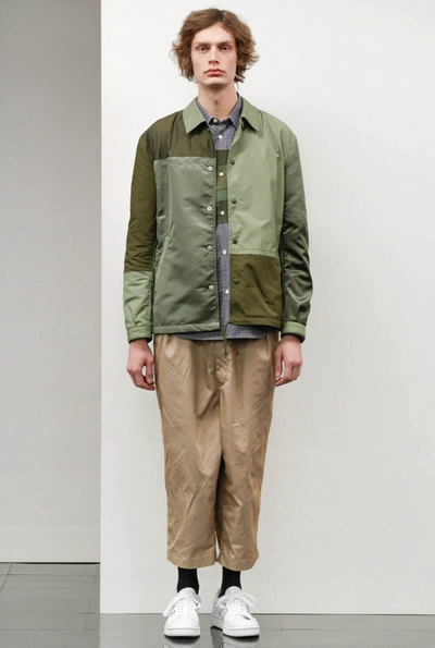 A man wearing a green Comme Des Garcons jacket with brown pants