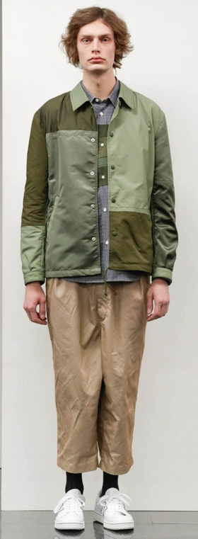 A man wearing a green Comme Des Garcons jacket with brown pants