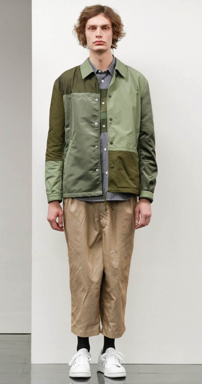 A man wearing a green Comme Des Garcons jacket with brown pants