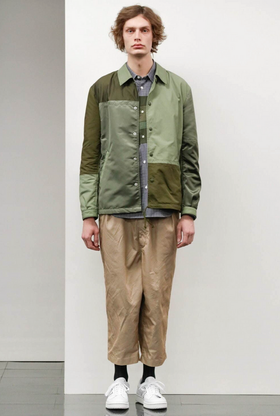 A man wearing a green Comme Des Garcons jacket with brown pants