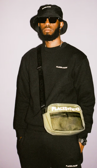 A man wearing a Places+Faces black crewneck, matching bucket hat and branded side-bafg