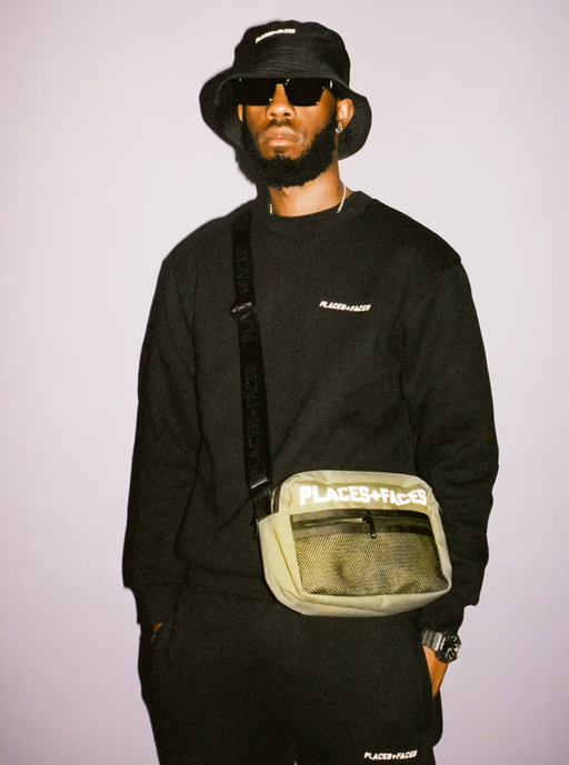 A man wearing a Places+Faces black crewneck, matching bucket hat and branded side-bafg