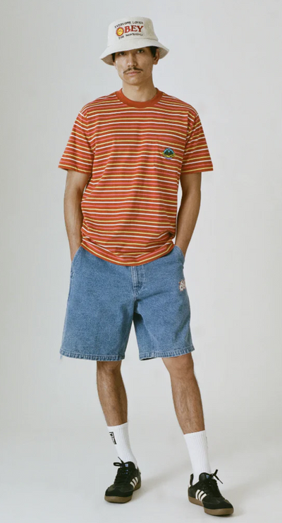 A man wearing a striped obey t-shirt with a branded bucket hat and denim shorts