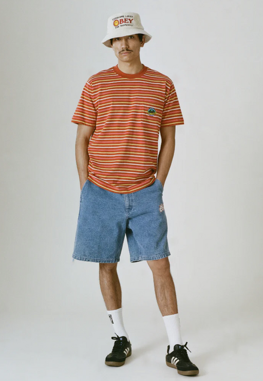 A man wearing a striped obey t-shirt with a branded bucket hat and denim shorts