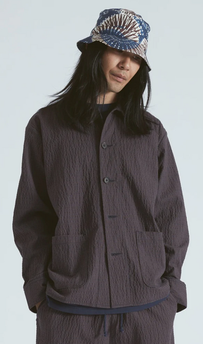 A man wearing a full Universal Works dark outfit with a graphic button up