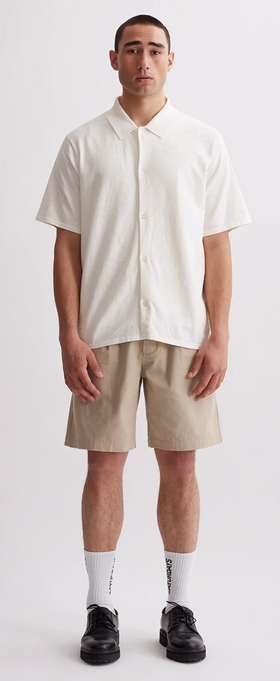 A man wearing a Saturdays NYC outfit featuring a short-sleeve button up and beige shorts