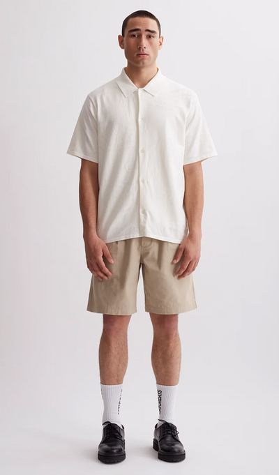 A man wearing a Saturdays NYC outfit featuring a short-sleeve button up and beige shorts