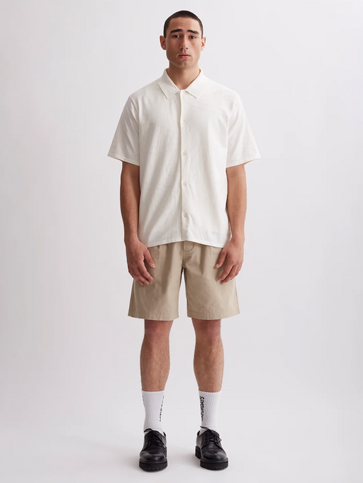 A man wearing a Saturdays NYC outfit featuring a short-sleeve button up and beige shorts