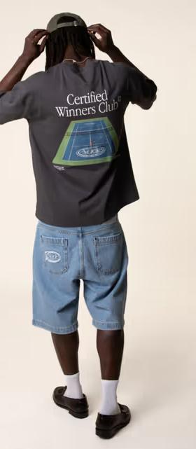 A man wearing a Nude Project tennis t-shirt with denim shorts