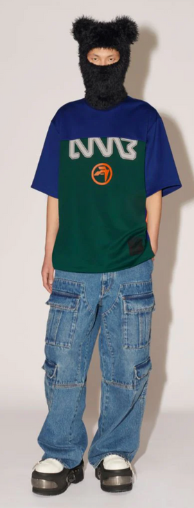 A woman wearing a Ambush outfit featuring a graphic t-shirt, jeans and a full face beanie