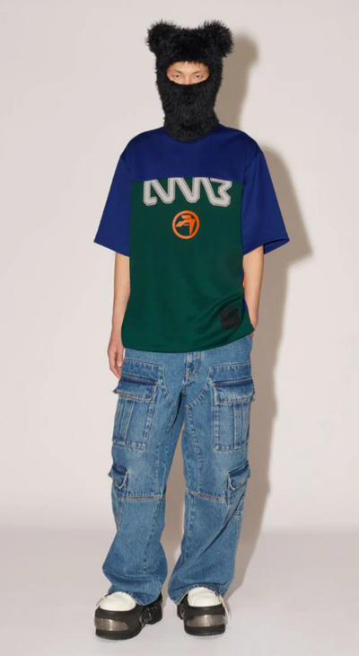 A woman wearing a Ambush outfit featuring a graphic t-shirt, jeans and a full face beanie