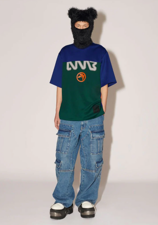 A woman wearing a Ambush outfit featuring a graphic t-shirt, jeans and a full face beanie