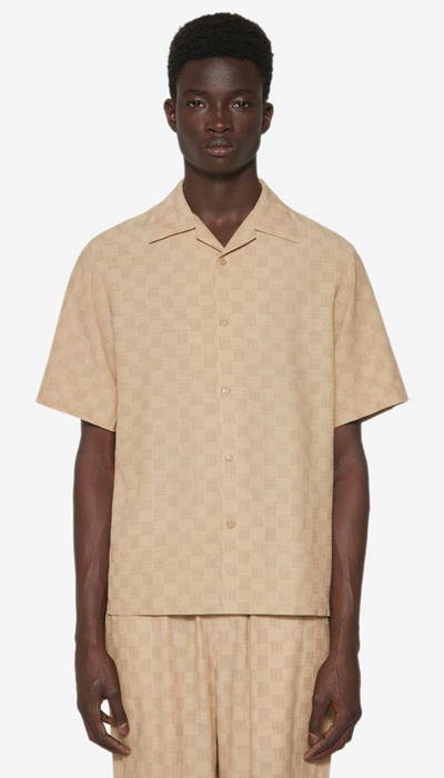 A man wearing a beige all over print MISBHV outfit with a matching shirt and pants