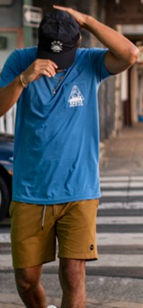 A man wearing a bright blue RVCA t-shirt, blue hat and brown bathing suit