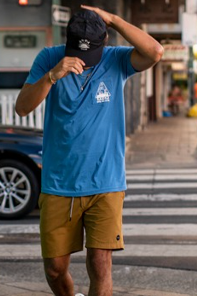 A man wearing a bright blue RVCA t-shirt, blue hat and brown bathing suit