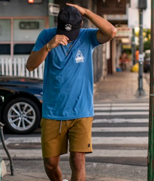 A man wearing a bright blue RVCA t-shirt, blue hat and brown bathing suit