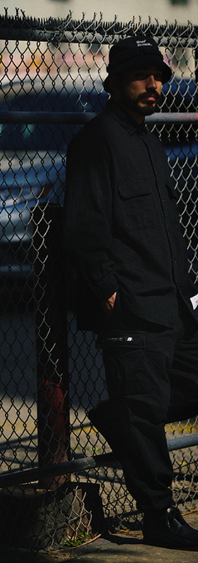 A man wearing a black WTAPS outfit with matching bucket hat
