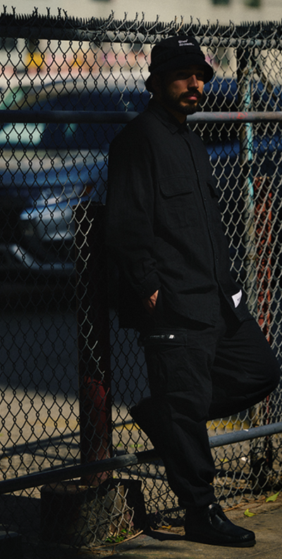 A man wearing a black WTAPS outfit with matching bucket hat