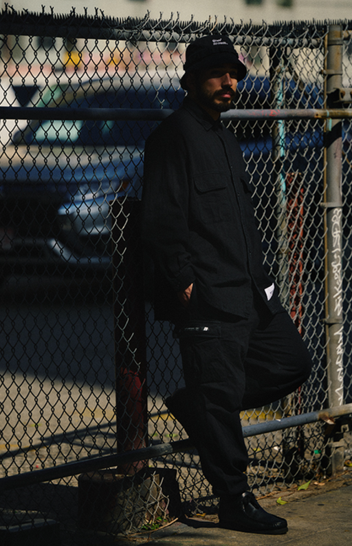 A man wearing a black WTAPS outfit with matching bucket hat
