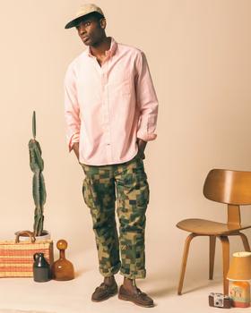 A man wearing a Gitman Vintage outfit featuring a pink button up shirt and camo pants
