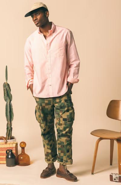 A man wearing a Gitman Vintage outfit featuring a pink button up shirt and camo pants