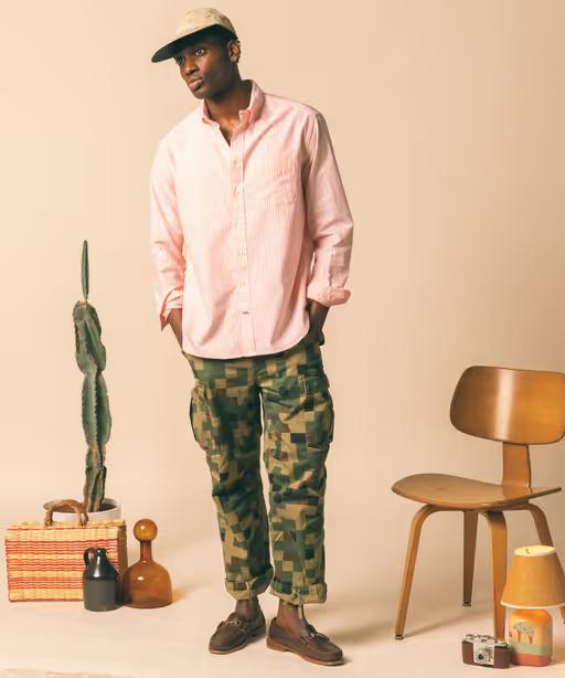 A man wearing a Gitman Vintage outfit featuring a pink button up shirt and camo pants