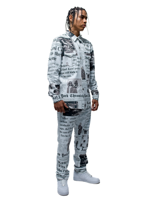 A man wearing an allover newsprint button up and pants done by Karl Kani
