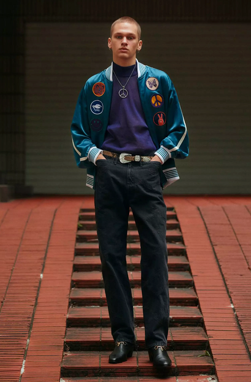 A man wearing a Needles jacket with peace prints allover it and black pants