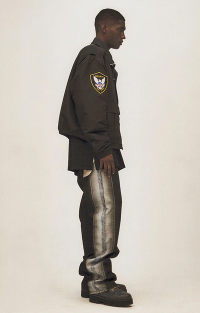 A man wearing a Heron Preston outfit featuring a coaches jacket and baggy jeans